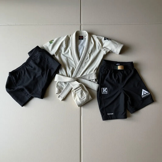 Grappling gi top and pants with rashguard and training shorts laid on a mat, showing fabric texture.